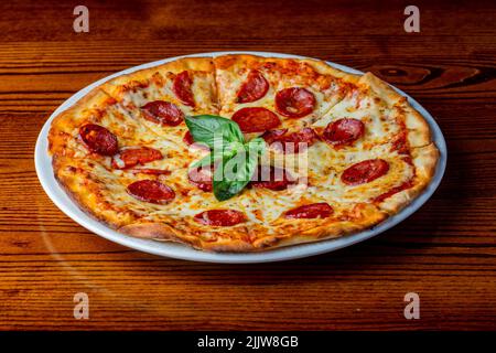 Un gros plan d'une pizza au pepperoni classique servi avec des feuilles de basilic. Banque D'Images