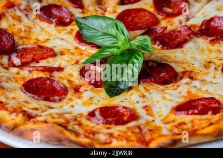 Un gros plan d'une pizza au pepperoni classique servi avec des feuilles de basilic. Banque D'Images