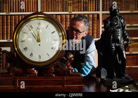 L'horologue Jonathan Betts inspecte une horloge en acajou Chippendale vers 1790, à l'intérieur de la bibliothèque de Stourhead House National Trust, dans le Wiltshire, où tous les anciens articles d'horlogerie exposés au public ont été liquidés pendant la pandémie et sont maintenant en cours de service, de blessure et de vérification, ainsi, ils peuvent à nouveau marquer et sonner en tant que chronométreurs fonctionnels et historiques. Date de la photo: Jeudi 28 juillet 2022. Banque D'Images
