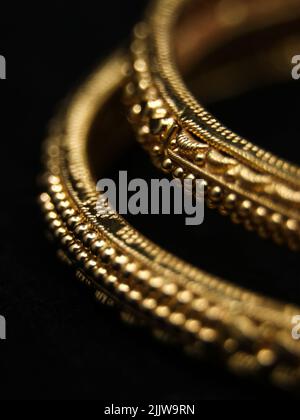 vintage golden bangles with ornate details carved captured in a closeup macro photo isolated in a black background Stock Photo