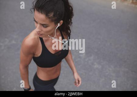 Athlète féminine musclée écoutant de la musique et marchant le long d'une route. Jeune femme sportive ayant une séance d'entraînement le matin. Banque D'Images