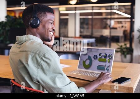 Un jeune homme d'affaires afro-américain souriant parle au téléphone tout en planifiant une stratégie sur ordinateur portable Banque D'Images