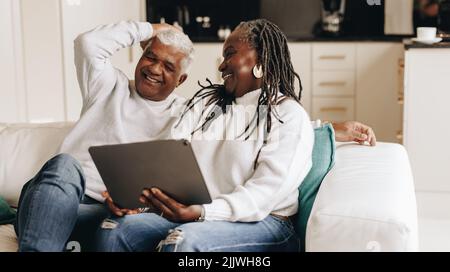 Un couple de personnes âgées heureux riant avec joie tout en utilisant une tablette numérique ensemble. Couple senior insouciant qui navigue sur Internet tout en se relaxant sur un canapé. Banque D'Images