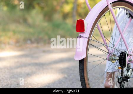 Gros plan vue rognée du vélo rose depuis l'arrière avec une femme qui la monte sur la route avec la nature et les plantes Banque D'Images