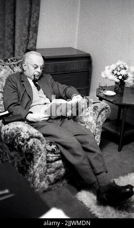 1960s, historique, homme âgé en costume, cravate et gilet, assis dans une chaise longue à motifs lisant un livre et fumant une pipe, Angleterre, Royaume-Uni. Un grand cabinet de gramophone est à côté de lui. Banque D'Images