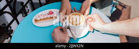 Vue rognée d'un vendeur mettant du cappuccino près d'eclair et d'une femme afro-américaine sur la terrasse d'un magasin de sucreries, bannière Banque D'Images