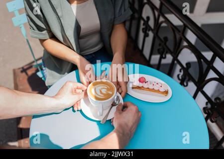 Vue rognée du vendeur mettant le café sur la table près d'eclair et client afro-américain sur la terrasse du café Banque D'Images