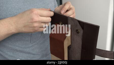 Homme travaillant avec le cuir par aiguille. Outils de couture pour sacs, portefeuilles, pochettes. Assemblage. Banque D'Images