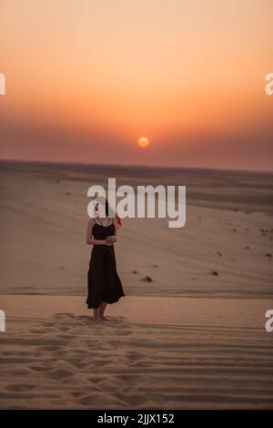 Femme en robe noire se promenant sur le sable tout en passant du temps dans le désert au lever du soleil à Doha, Qatar Banque D'Images