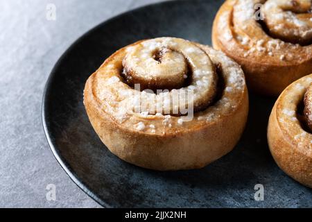 Petits pains à la cannelle Kanelbulle dessert suédois traditionnel servi dans une assiette noire Banque D'Images