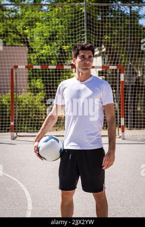 Jeune joueur de football masculin regardant loin en se tenant debout avec le ballon sur le terrain Banque D'Images