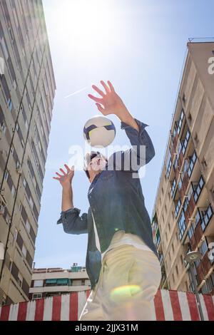 Vue en contre-angle d'un jeune homme jouant avec le football contre le ciel pendant une journée ensoleillée Banque D'Images