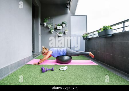 Profil de femme âgée en équilibre sportif sur le ballon de sport au balcon Banque D'Images
