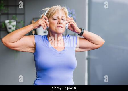 Femme sportive senior pratiquant le yoga tout en écoutant de la musique sur un casque Banque D'Images