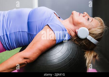 Vue latérale d'une femme âgée souriante qui porte un casque et qui se penche sur le ballon lors de l'entraînement Banque D'Images