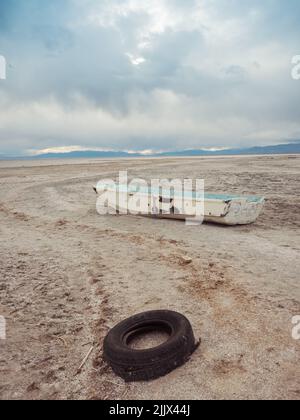 Bateau endommagé et pneu déchiré placé sur un bord de mer sablonneux contre ciel gris nuageux le jour de tempête sur Bombay Beach en Californie, États-Unis Banque D'Images