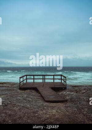 Promenade et plate-forme de bois avec balustrade située sur une côte rocailleuse agitée contre la mer et le ciel gris nuageux le jour de tempête à Rias Baixas, Espagne Banque D'Images