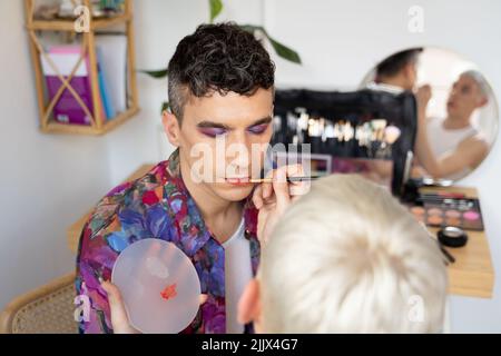 Jeune homme androgyne se maquiller fait par son petit ami à la table de dressing Banque D'Images