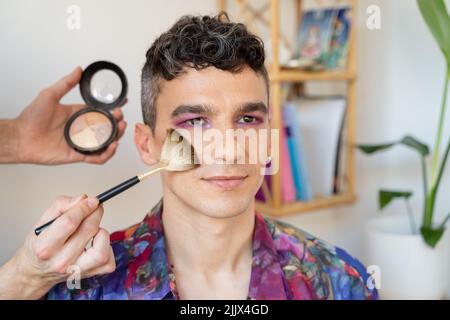 Gros plan de l'homme transgenre qui se fait rougir avec la brosse à maquillage Banque D'Images