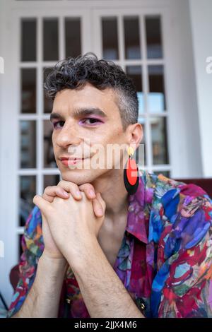 Portrait d'un gay heureux portant des boucles d'oreilles et se penchant sur les mains classées à la maison Banque D'Images