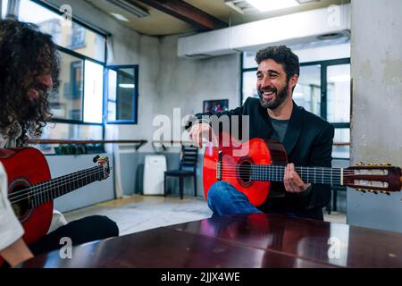 Des amis de sexe masculin jouant des guitares à table dans un studio de musique Banque D'Images