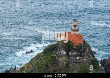 Falaise rocheuse avec phare situé près de la mer interminable de tempête contre le ciel couvert dans la zone côtière de l'Espagne le jour d'été Banque D'Images