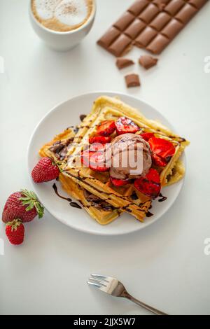 Des gaufres maison savoureuses sont servies sur l'assiette avec boule de glace au chocolat et à la fraise et sauce près de la tasse avec café dans un kit léger Banque D'Images