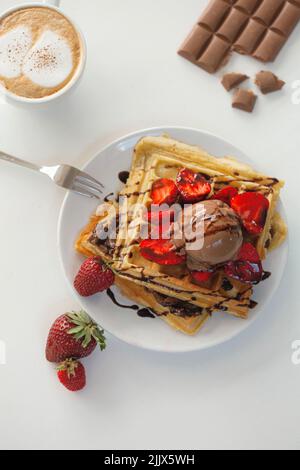 Des gaufres maison savoureuses sont servies sur l'assiette avec boule de glace au chocolat et à la fraise et sauce près de la tasse avec café dans un kit léger Banque D'Images