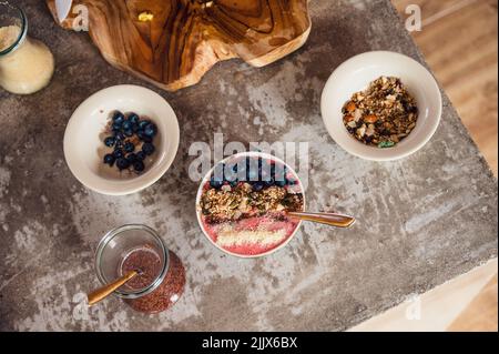 Vue de dessus d'un savoureux bol de smoothie rose frais avec bleuets sur la table avec granola et graines de lin imbibées dans la cuisine Banque D'Images