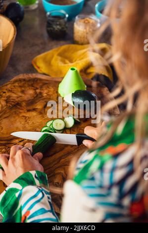 De dessus de la récolte anonyme femme cuire en coupant le concombre vert frais sur la planche à découper tout en cuisant la salade dans la cuisine légère Banque D'Images