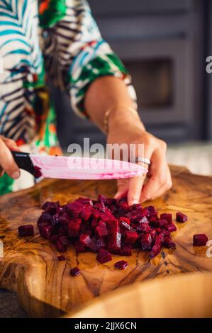 Une femelle méconnaissable hache-betterave bouillie avec un couteau en céramique sur une dalle de bois tout en cuisinant un plat végétarien à la maison Banque D'Images