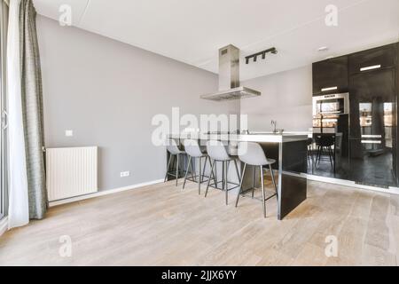 Intérieur de cuisine ouverte contemporaine avec comptoirs noirs et appareils dans spacieux appartement lumineux avec îlot et tabourets Banque D'Images