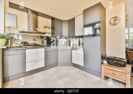 Cuisinière et four en chrome dans une cuisine ancienne avec mobilier gris et sol carrelé dans un appartement lumineux Banque D'Images