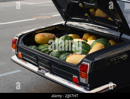 Angle élevé de melons mûrs et de pastèques à vendre placé dans le coffre ouvert de véhicule noir d'époque stationné sur la route asphaltée sur la rue de la ville Banque D'Images