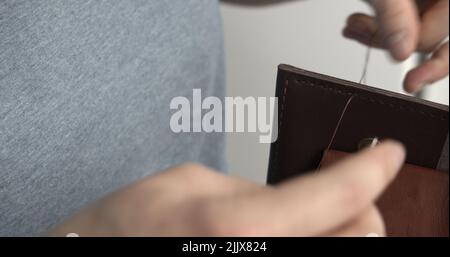 Fabrication d'un portefeuille en cuir marron fait main. Les mains du maître coudre un produit en cuir. Banque D'Images