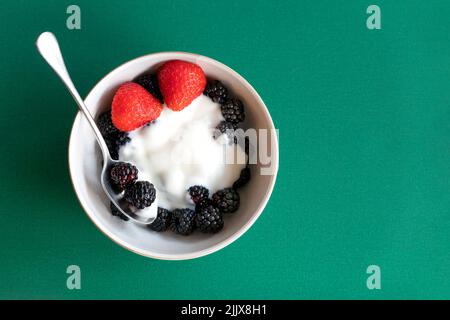 Un petit bol de désert plein de mûres sauvages fraîchement cueillies, couvert de yaourt grec et habillé d'une fraise fendue. Un repas nutritif Banque D'Images