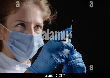 Une femme médecin portant un masque de protection et des gants tient une seringue avec un vaccin ou une injection sur un fond noir. Une infirmière prépare Banque D'Images