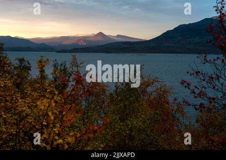 Le soleil se lève dans le brouillard, ce qui rend le ciel jaune, et illumine les sommets spectaculaires des montagnes au-dessus du lac, dans le paysage arctique lointain de Stora Sjofallet National Banque D'Images