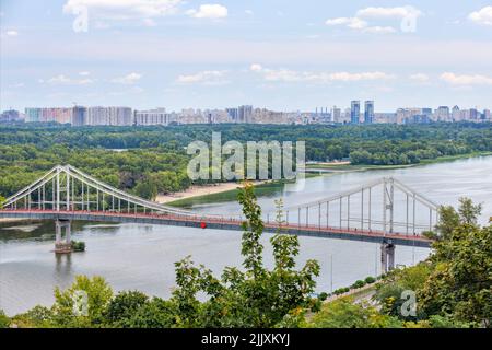 Pont piétonnier traversant la rivière Dnipro jusqu'à la plage de l'île de Trukhanovy à Kiev, en été, surplombant un parc de loisirs verdoyant. Banque D'Images