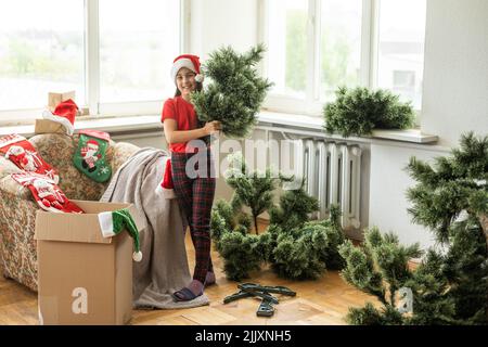 Photo de petite fille gaie mignonne fait un arbre de Noël artificiel porter chapeau de santa à l'intérieur Banque D'Images