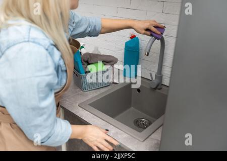 Les gens, les travaux ménagers et le concept de ménage.Blonde femme d'âge moyen avec bouteille de nettoyant spray four avec éponge à la cuisine à la maison. Banque D'Images