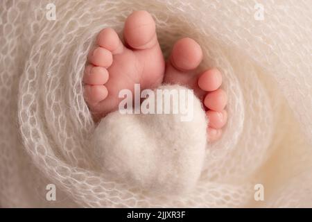 Coeur blanc tricoté dans les jambes d'un bébé. Pieds doux d'un nouveau-né dans une couverture de laine blanche. Banque D'Images