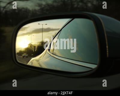 Vue arrière : le flanc d'un Aston Martin Vantage se reflète dans son miroir d'aile sur une autoroute au coucher du soleil Banque D'Images