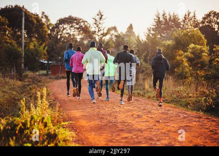 Entraînement matinal au Kenya. Un groupe de coureurs d'endurance courent sur le sol rouge au lever du soleil. Motivation de course matinale pour l'entraînement. Banque D'Images