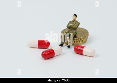 Une figurine miniature d'un homme se trouve sur des pièces de monnaie à côté de ses capsules médicales. Coûts de traitement Banque D'Images