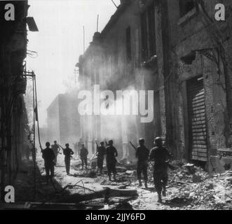 Recherche de tireurs d'élite -- Une unité de reconnaissance se déplace dans une rue de Messine, en Sicile, à la recherche de tireurs d'élite ennemis alors que les forces alliées entrent dans la ville. La fumée des bâtiments en feu est suspendue au-dessus de la rue aux débris. 24 août 1943. (Photo par AP Wirephoto). Banque D'Images