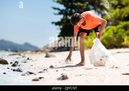 Déchets de plastique. Pollution des mers et des océans. Nettoyage de la plage. Jeune homme cueillant des bouteilles en plastique utilisées sur le sable. Banque D'Images
