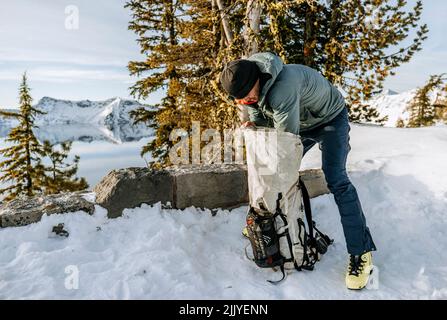 Le skieur charge un sac à dos en hiver tout en campant près du lac Crater. Banque D'Images