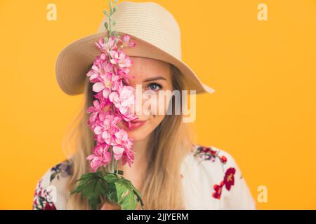 fille caucasienne portant un chapeau et tenant une fleur regardant la caméra sur fond orange . Photo de haute qualité Banque D'Images