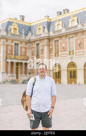 Un jeune homme en lunettes se tient devant le château de Versailles Banque D'Images